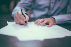 Person signing a document with a pen
