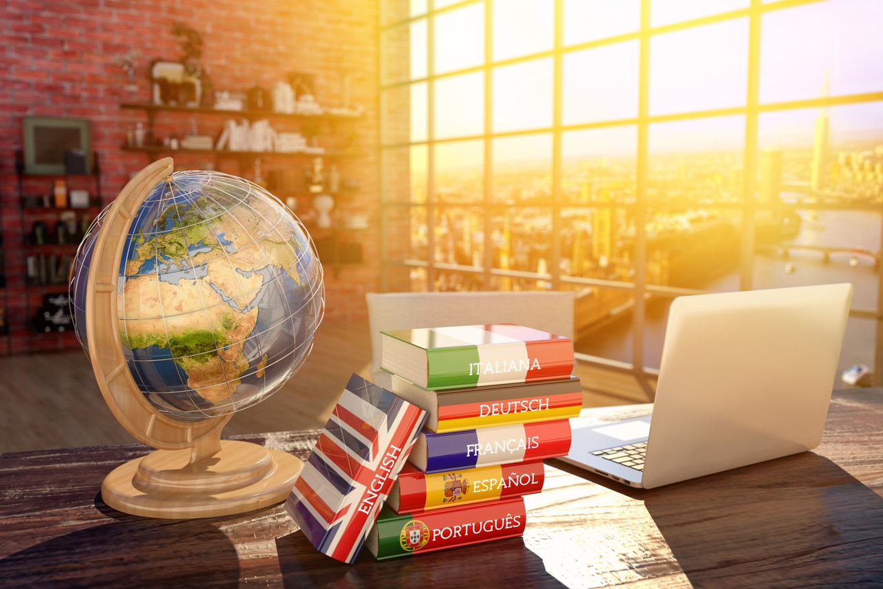 Globe, laptop and a stack of language dictionaries on a sunlit desk