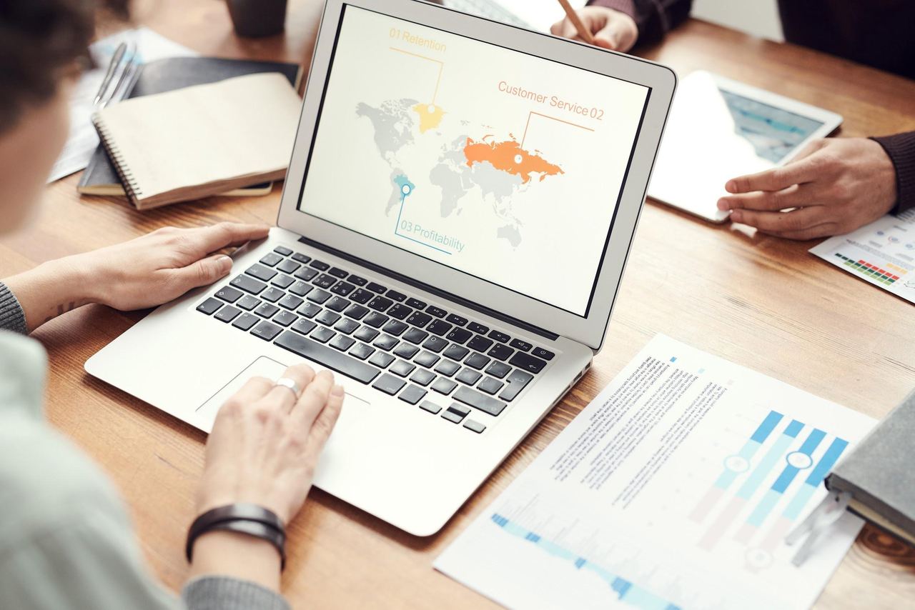 Laptop showing a world map with international markets highlighted, next to printed business charts