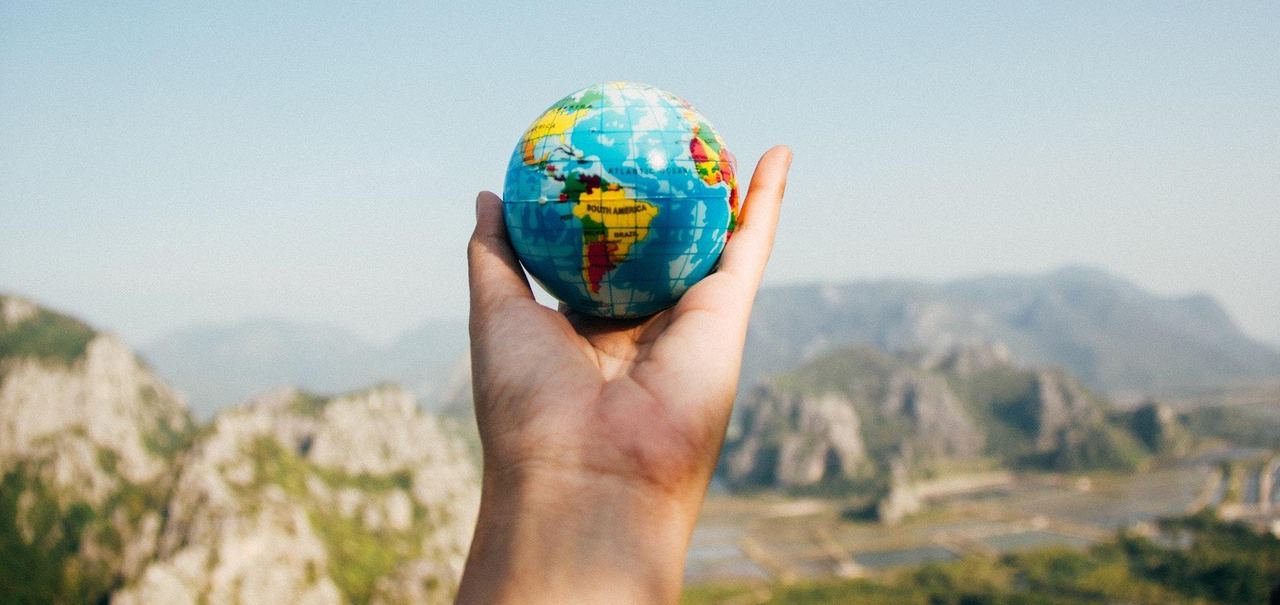 Hand holding a small globe against a mountain landscape