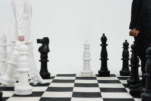 Giant black and white chess pieces facing each other on a floor-sized chessboard